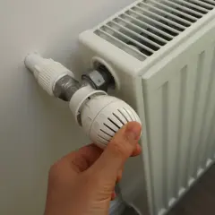 Ręka reguluje termostat grzejnika, gdy zaczynają grzać w blokach.