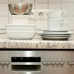 Zmywarka Whirlpool z kodami błędów. Stos naczyń na blacie, obok gniazdka elektrycznego.