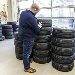Mężczyzna wybiera najlepsze opony spośród wielu stosów. W magazynie panuje porządek, a opony są ułożone w równych rzędach.