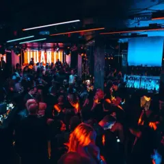 Una folla balla in una discoteca illuminata da luci al neon, un DJ suona musica elettronica. Sembra una delle migliori discoteche techno in Italia.