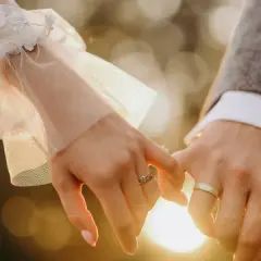 Dłonie pary młodej splatają się w romantycznym geście. Delikatna koronka sukni ślubnej i elegancki garnitur świadczą o tym, że to ich ślub bez wesela, pełen intymności i miłości.