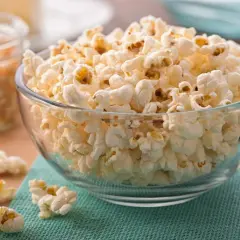 Puszysty popcorn na patelni, gotowy do chrupania. W tle widać nasiona kukurydzy.