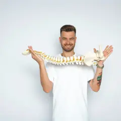 Uśmiechnięty mężczyzna trzyma model kręgosłupa, wyjaśniając, whiplash co to jest.