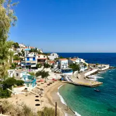 En pittoresk kustby på Ikaria, Grekland, med vita hus, en sandstrand och turkost vatten.