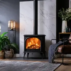 Poêle à bois en fonte, cœur de la pièce, réchauffant l'atmosphère. Un fauteuil en cuir invite à la détente.