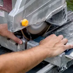 Hands guide a tile across a wet saw, demonstrating how to cut tile that is already installed.