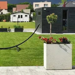 Nowoczesny ogród z zadbanym trawnikiem, betonową donicą, drzewkiem i czarną altaną.