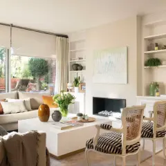Salón moderno con sofá beige, mesa de centro blanca, chimenea y dos sillones con estampado de cebra.