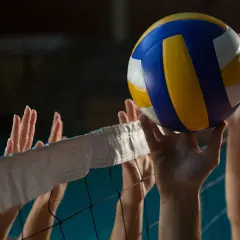 Piłka do siatkówki tuż nad siatką, ręce graczy gotowe do akcji. Zastanawiasz się, ile trwa mecz siatkówki?
