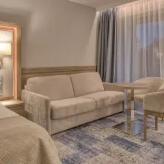 Przytulny pokój w hotelu 5 gwiazdkowym nad morzem: wygodna sofa, stolik z krzesłami i łóżko.