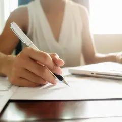 Osoba pisze długopisem na papierze, obok laptopa. Tworzy regulamin grupy na FB, dbając o szczegóły.
