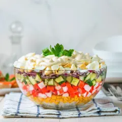 Deliciosa ensalada de surimi en capas, con maíz, pepino, cebolla morada y huevo duro, cubierta de mayonesa y perejil.