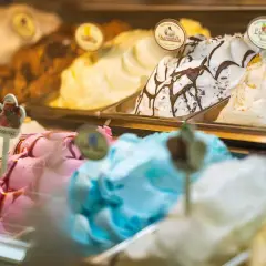Verschiedene Eissorten in einer Auslage, darunter ein cremiges gelbes Eis, Stracciatella und ein fruchtiges Eis.