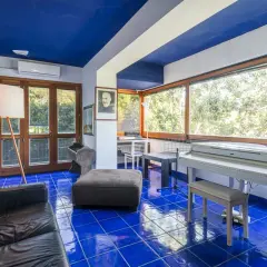 Interno con pavimento blu brillante, pianoforte bianco, divano nero e un ritratto di Padre Pio, come in testi lucio dalla la casa in riva al mare.
