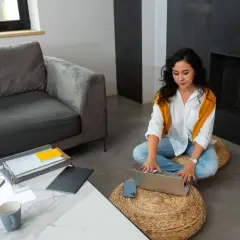 Mujer trabajando en portátil en el salón, pensando si puedo alquilar mi vivienda habitual.