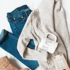 Un jean, un pull torsadé, une tasse et une botte en daim : un parfait style vestimentaire hiver pour une journée cosy.