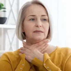 Kobieta z rękami na szyi, odczuwająca dyskomfort związany z ciągłym chrząkaniem i wydzieliną w gardle.