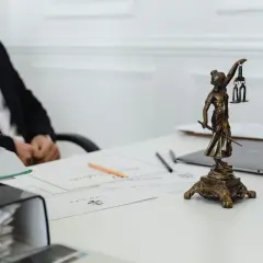 Une statue de la justice, symbole du juge de l'exécution, trône sur un bureau avec des documents et un homme en costume.