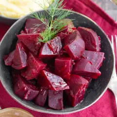Schüssel mit gewürfelten, glänzenden roten Rüben, die man roh essen kann, garniert mit Dill. Daneben Kartoffelpüree und Besteck.