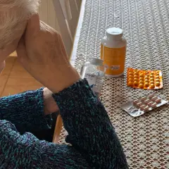 Osoba w swetrze z lekami na stole. Zastanawia się, renta wdowia komu przysługuje, szukając odpowiedzi.