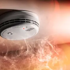 Detector de humo en el techo, rodeado de humo. Ilustra cómo funciona un detector de humo al alertar sobre el peligro.