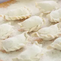 Surowe pierogi, gotowe do gotowania, posypane mąką. Idealne na domowy obiad, zgodnie z tradycyjnym ciasto na pierogi przepisem.