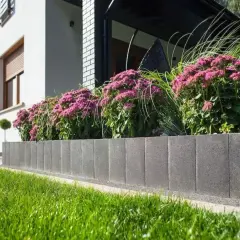 Nowoczesne donice z palisady przed domem, pełne kwitnących, różowych kwiatów i traw ozdobnych, tworzą piękny kontrast z bielą elewacji.