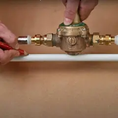 Ajustement d'un réducteur de pression pour comment augmenter la pression d'eau. Un homme marque un tuyau avec un crayon.