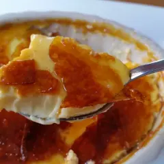 En sked tar en bit av en krämig creme brulee med karamelliserat sockerlock.