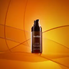 En flaska Medik8 C-Tetra Advanced serum med 20% C-vitamin, en kraftfull antioxidant för din hudvård, står på en orange bakgrund.