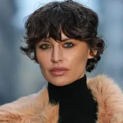 Ein modischer Pixie Cut mit feinem Haar betont die grünen Augen einer Frau in einem Pelzmantel.