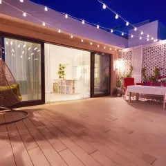 Terraza con silla colgante y mesa, iluminada por una guirnalda de luces. La pantalla lámpara plisada ilumina el ambiente.