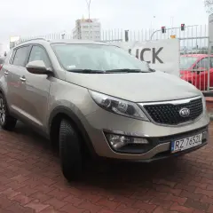 Złoty Kia Sportage 2012 na czerwonej kostce brukowej, z tablicą rejestracyjną RZ 7652L.