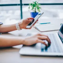 Kobieta korzysta z telefonu i laptopa, szukając informacji, jak podłączyć internet z telefonu do komputera.