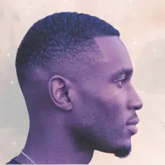Perfil de hombre con un corte de pelo tuper fade, ondas definidas y barba corta.
