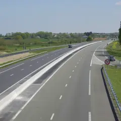 Vue aérienne d'une autoroute avec une voie d'accélération et de décélération, bordée de verdure et de panneaux de signalisation.