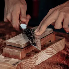 Manos afilando un cuchillo en una piedra de afilar. El filo cuchillo recupera su brillo y precisión.