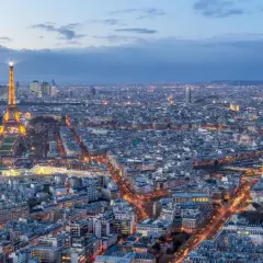 Vue panoramique de Paris au crépuscule, avec la Tour Eiffel illuminée et le dôme des Invalides. On aperçoit le quartier de La Défense au loin. Un panorama depuis l'**étage tour Montparnasse**.