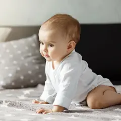 Urocze dziecko w białym body, kiedy dziecko raczkuje, z zaciekawieniem spogląda w bok.