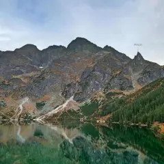 Majestatyczny Mnich w Tatrach góruje nad spokojnym jeziorem, odbijając się w jego zielonych wodach.