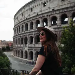 Une femme avec un chapeau et des lunettes de soleil admire le Colisée. Je visite Rome et ce moment est inoubliable.
