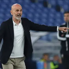 Trener Stefano Pioli w garniturze i białej koszulce polo wskazuje palcem, udzielając wskazówek na boisku.