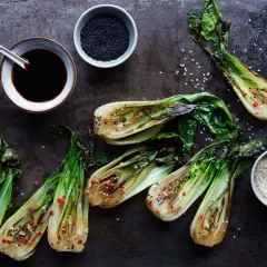 Grillad pak choi med sesamfrön och chili. En skål med sojasås och en skål med svarta sesamfrön syns också.