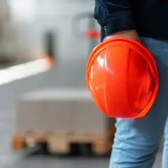 Persona con casco arancione in mano, in un magazzino. Il RSPP quando è obbligatorio garantisce la sicurezza.