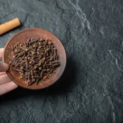 Un plato de clavo de olor, un remedio natural para el dolor de muelas, junto a dos ramas de canela sobre una superficie oscura.