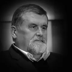 Portret Andrzeja Zielińskiego, mężczyzny z siwą brodą i zmarszczkami, w czarnym garniturze.
