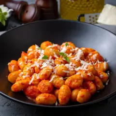 Gnocchi di ceci e patate conditi con sugo rosso e parmigiano grattugiato, guarniti con basilico fresco.