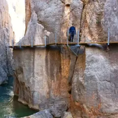 Un excursionista camina por las pasarelas de Valloré, un sendero suspendido sobre un río turquesa entre imponentes paredes rocosas.