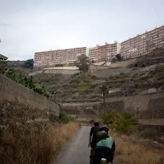 Ciclistas recorren el **barranco de Guiniguada**, con edificios residenciales en la ladera y vegetación seca.