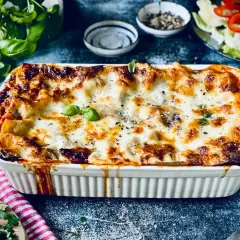 Herzhafte vegetarische Lasagne mit geschmolzenem Käse und frischem Basilikum, serviert in einer weißen Auflaufform.